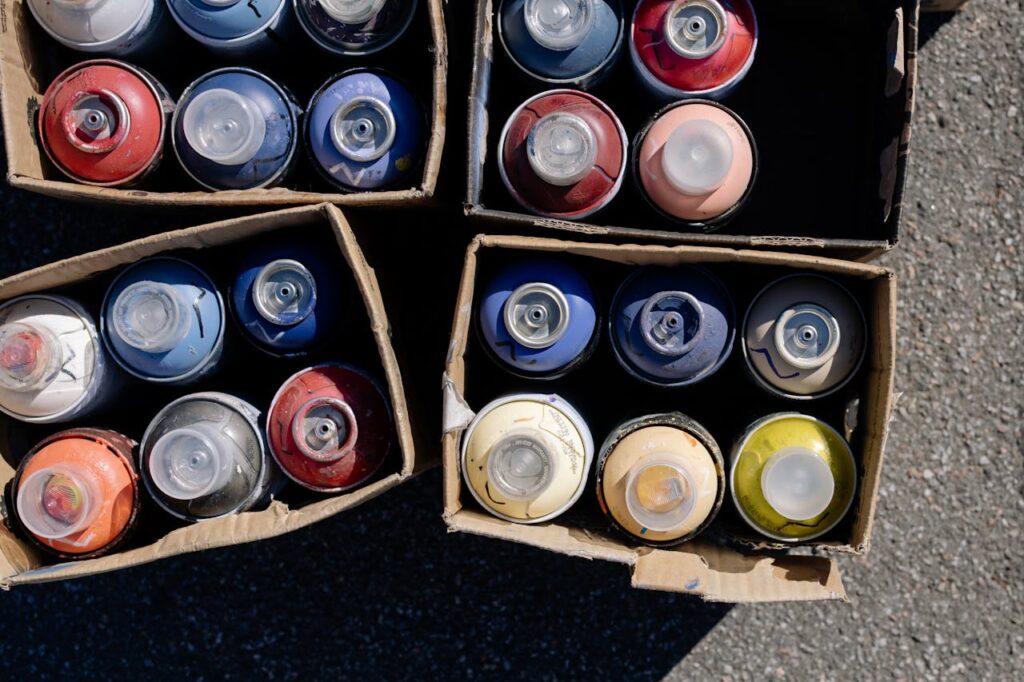 High-angle view of colorful spray paint cans organized in cardboard boxes outdoors.